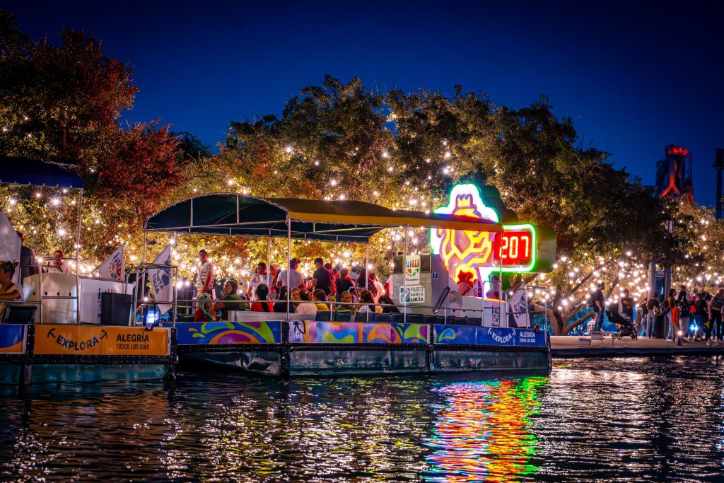 Barco turístico del Paseo Santa Lucía lleno de visitantes junto a un letrero de neón por la noche