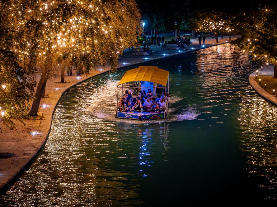 Barco turístico navegando de noche por el canal entre árboles cubiertos de luces cálidas