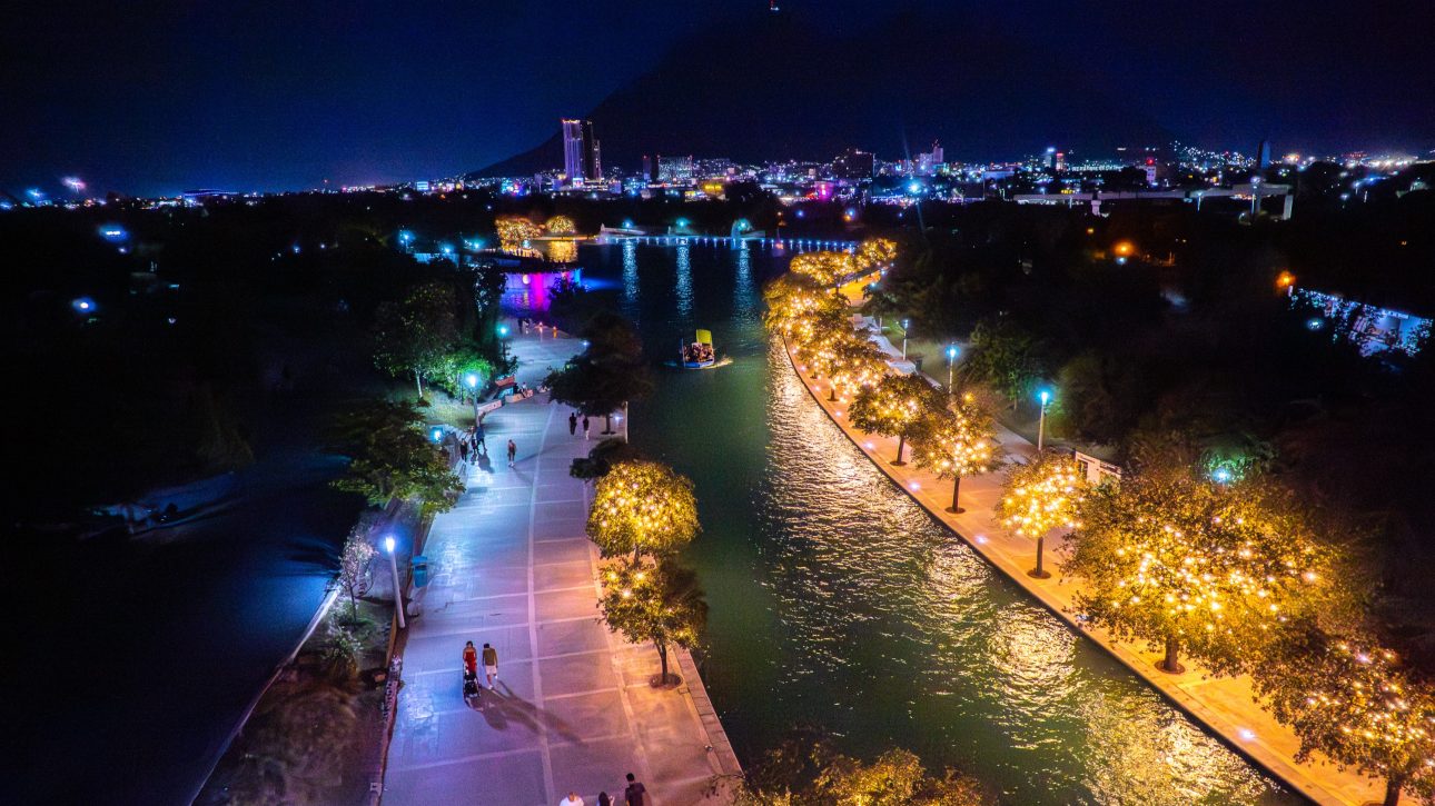 Vista nocturna del canal del Paseo Santa Lucía con barco turístico, árboles iluminados y la ciudad al fondo.