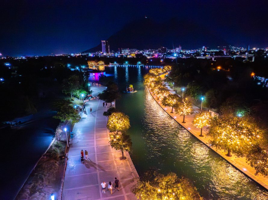 Vista nocturna del canal del Paseo Santa Lucía con barco turístico, árboles iluminados y la ciudad al fondo.