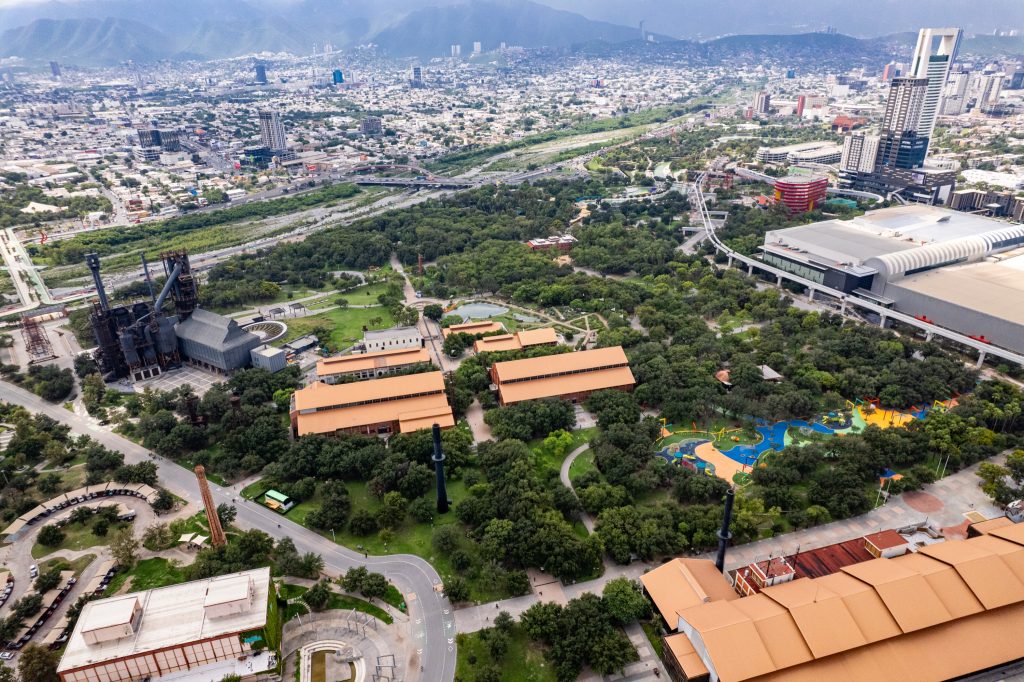 Vista aérea del parque con el alto horno de acero, naves de techo naranja y área de juegos infantiles